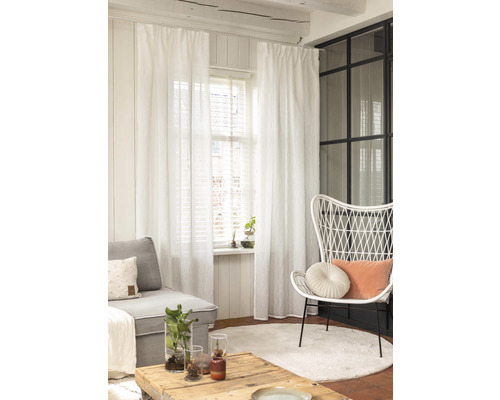 Wohnzimmer mit Sofa, Sessel, Tisch, Teppich und weißen Gardinen.