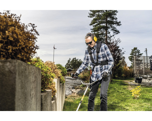 Un homme portant des lunettes de protection et un casque antibruit utilise un coupe-bordures dans le jardin.