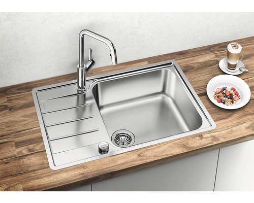 Spüle aus Edelstahl mit Abtropffläche und Armatur auf einer hölzernen Arbeitsplatte