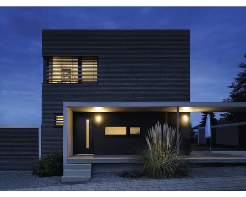Modernes Haus mit Holzfassade, Carport und Beleuchtung bei Dämmerung.