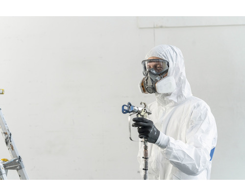 Eine Person in Schutzkleidung, Schutzbrille und Atemschutzmaske hält eine Farbspritzpistole.