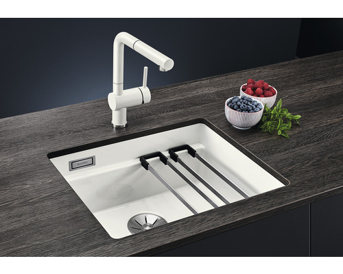 Évier de cuisine avec égouttoir et robinet sur un plan de travail foncé avec des bols de fruits rouges