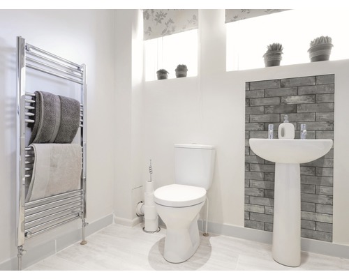 Salle de bain lumineuse avec toilettes, lavabo, radiateur et serviettes.
