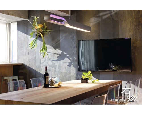 Salle à manger avec table en bois, chaises, lampe et télévision sur un mur en pierre.