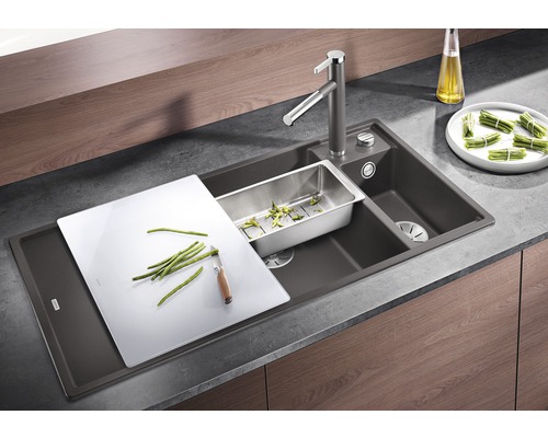 Évier avec égouttoir, planche à découper, passoire et robinetterie dans une scène de cuisine.