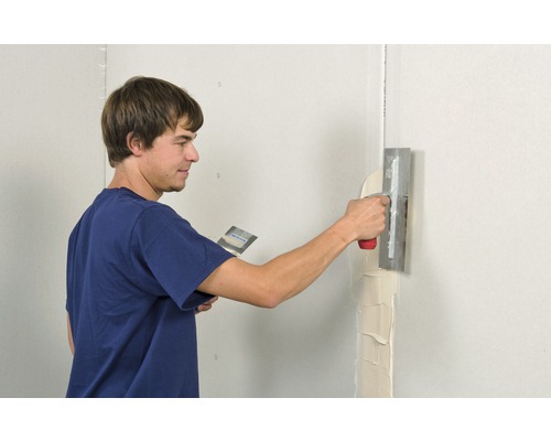 Mann spachtelt Wand mit Spachtel und Glättkelle