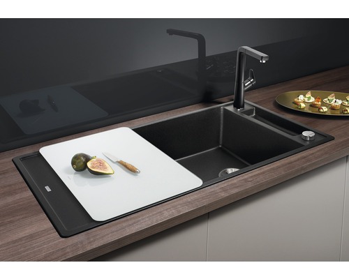 Évier de cuisine noir avec robinet, planche à découper, figues et couteau.