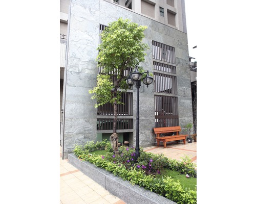 Außenansicht eines Gebäudes mit Baum, Blumenbeet, Straßenlaterne und Bank