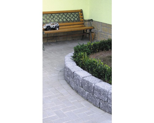 Scène de jardin avec un mur de pierre, un chemin pavé et un banc en bois