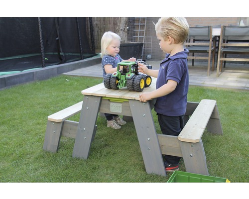 Kinder spielen an einem Picknicktisch aus Holz im Garten.