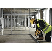 Ein Bauarbeiter befestigt eine Metallschiene mit einem Bohrer in einem Raum mit Metallrahmen.