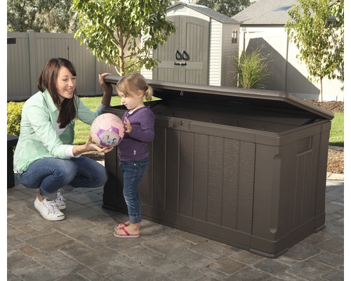 Coffre de jardin marron en plastique avec couvercle ouvert dans le jardin avec une femme et un enfant