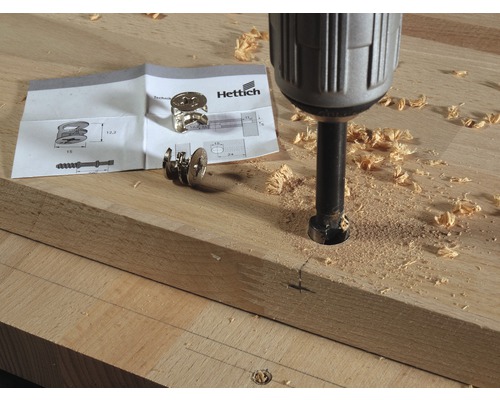 Perceuse perçant un trou dans une planche de bois à côté de la quincaillerie et des instructions