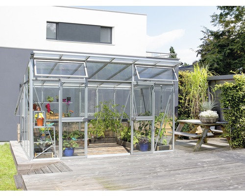 Serre avec plantes sur terrasse en bois devant une maison d''habitation.