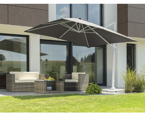 Scène de terrasse avec parasol déporté, salon de jardin en rotin et table basse sur pelouse devant une maison