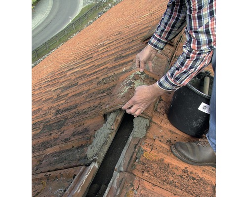 Ein Mann repariert ein Dach mit Dachziegeln und Mörtel.