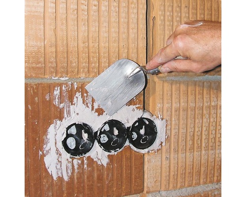 Artisan enduisant un mur en briques avec trois boîtes électriques noires