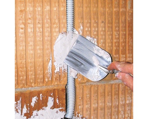 Un électricien enduit un mur avec une truelle.