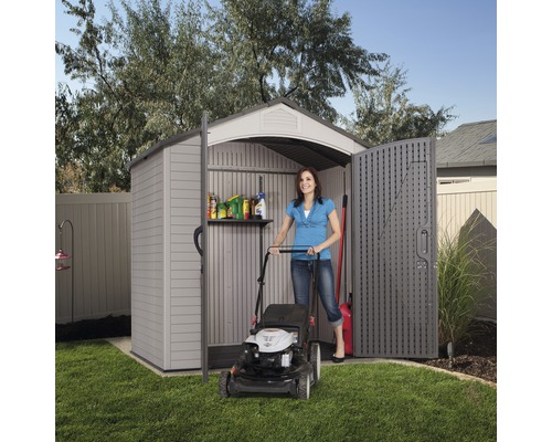 Frau schiebt Rasenmäher in Gartenhaus