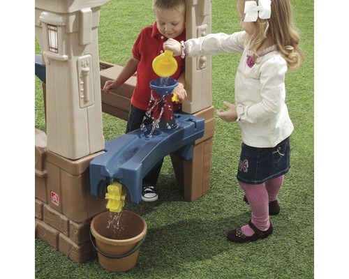 Zwei Kinder spielen mit einem Wasserspieltisch im Freien und schütten Wasser in einen Eimer.