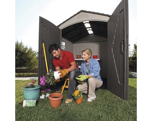 Scène de jardin avec un couple devant une cabane de jardin plantant des fleurs dans des pots