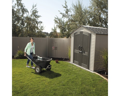 Femme poussant une brouette dans un jardin avec une remise.
