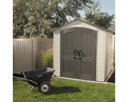 Scène de jardin avec une remise et une brouette sur une pelouse.