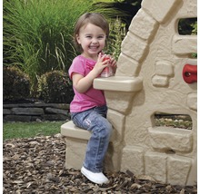 Une petite fille est assise près d''une cabane de jeu pour enfants dans le jardin.