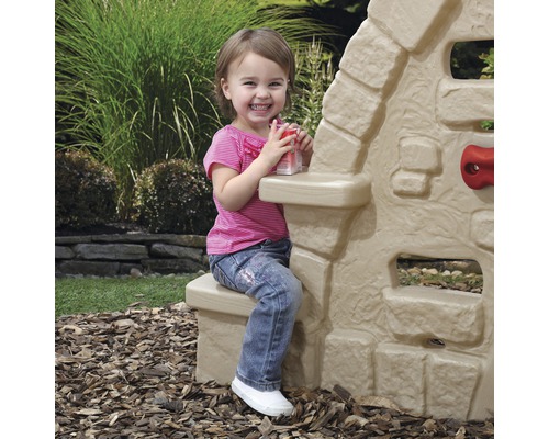 Ein kleines Mädchen sitzt an einem Kinderspielhaus im Garten.