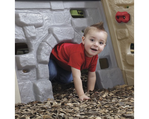 Ein Kind krabbelt durch einen Spieltunnel mit Kletterwand im Garten.