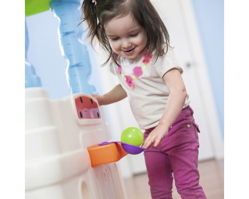 Une fille souriante joue avec une cuisine pour enfants et une balle.