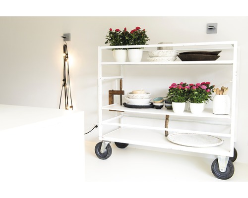 Étagère roulante blanche avec pots de fleurs, bols et objets décoratifs dans une pièce lumineuse.