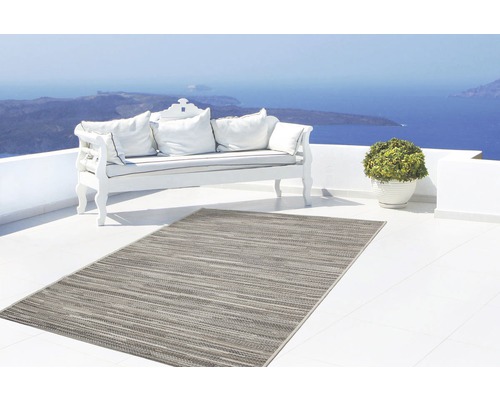 Szene mit einem grauen Outdoor Teppich, einer Bank mit Kissen und einer Pflanze auf einer Terrasse mit Meerblick.