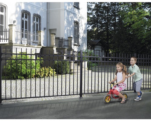Clôture métallique noire devant un bâtiment avec des enfants qui jouent