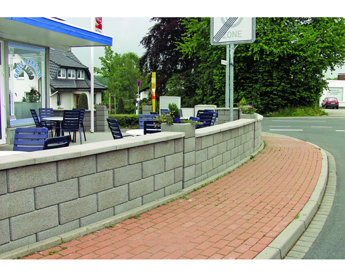 Eine graue Mauer aus Betonsteinen säumt den Weg vor einem Gebäude.