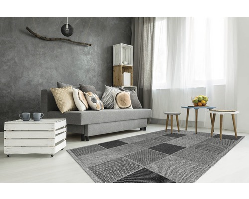 Wohnzimmer mit grauem Sofa, Couchtisch aus Holzkisten und Teppich mit quadratischem Muster