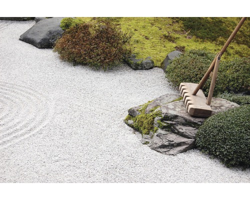 Zen-Garten mit Kiesfläche, Steinen, Moos, Büschen und Rechen
