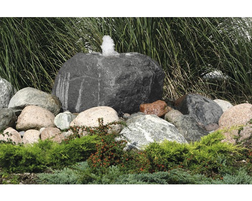 Gartenbrunnen aus Stein mit Wasserfontäne, umgeben von Steinen und Pflanzen