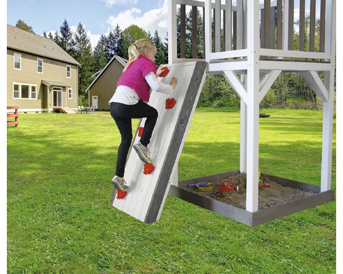 Kind klettert an einer Kletterwand eines Spielhauses im Garten.