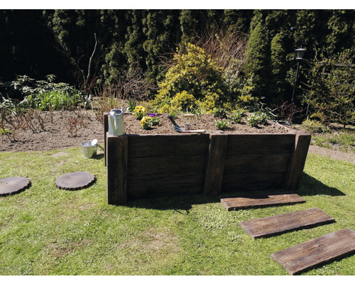 Hochbeet aus Holz im Garten mit Bepflanzung, Giesskanne und Gartengeräten