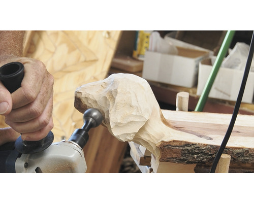 Eine Person verwendet eine Schleifmaschine, um eine Holzskulptur in Hundeform zu bearbeiten.