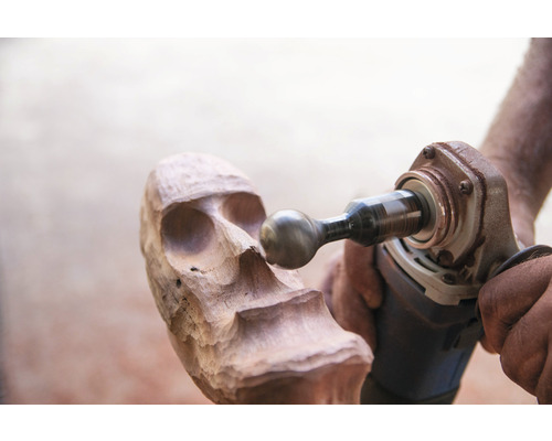 Holzbearbeitung mit Schleifwerkzeug an einer Holzskulptur in Schädelform.