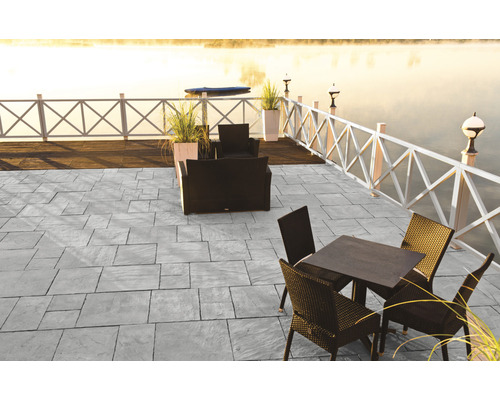 Terrasse mit grauen Steinplatten und Gartenmöbeln am See