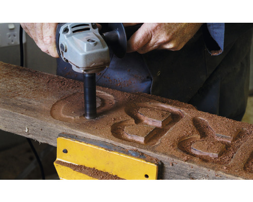 Eine Person verwendet einen Winkelschleifer zum Schnitzen von Herzformen in ein Holzbrett.