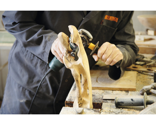 Person bearbeitet Holzskulptur mit Schleifwerkzeug