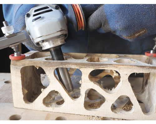 Eine Person bearbeitet ein Holzstück mit einer Oberfräse und einer Schablone