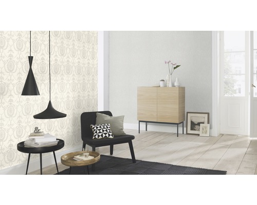 Salon lumineux avec papier peint à motifs, fauteuil, commode et suspensions.