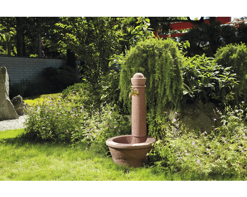 Fontaine de jardin en pierre avec robinet dans un jardin verdoyant.