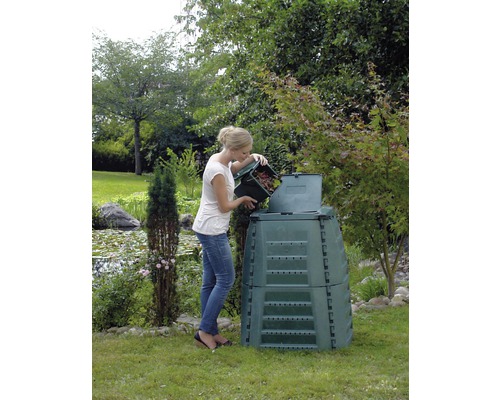 Une femme remplit un composteur avec des déchets de jardin dans le jardin.