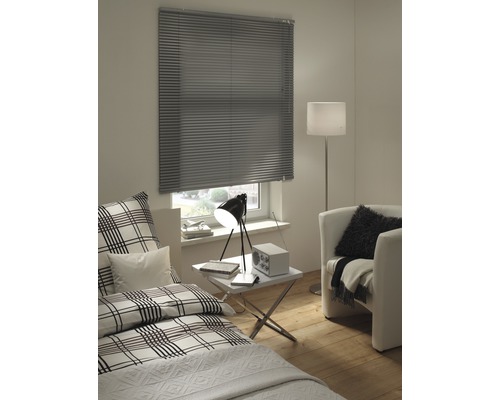 Zimmer mit Bett, Sessel und geschlossenem Fenster mit Jalousie.